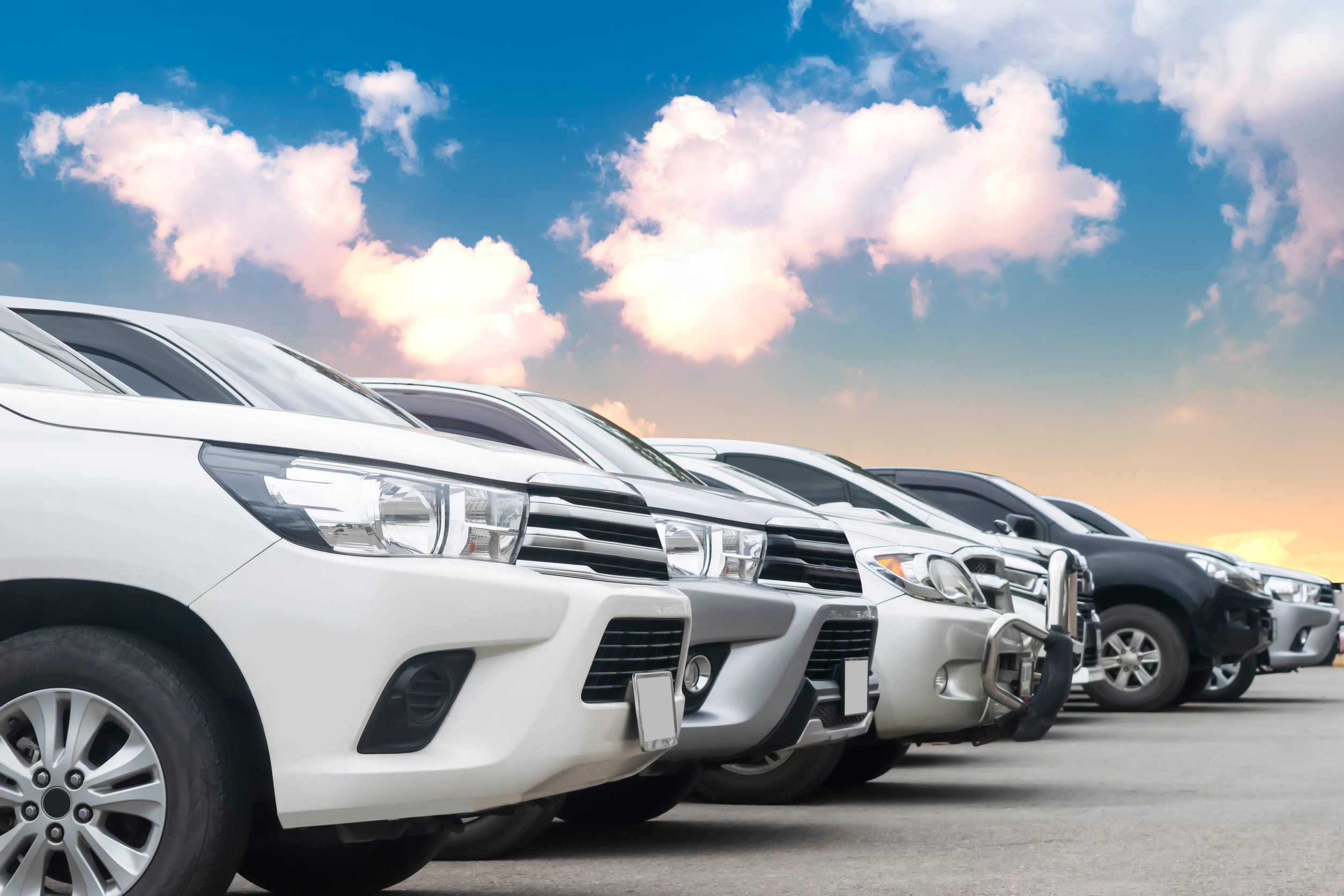 Cars parking in asphalt parking lot in a row with cloudy sky background in nature. Outdoor parking lot with fresh ozone, green environment of transportation and technology concept