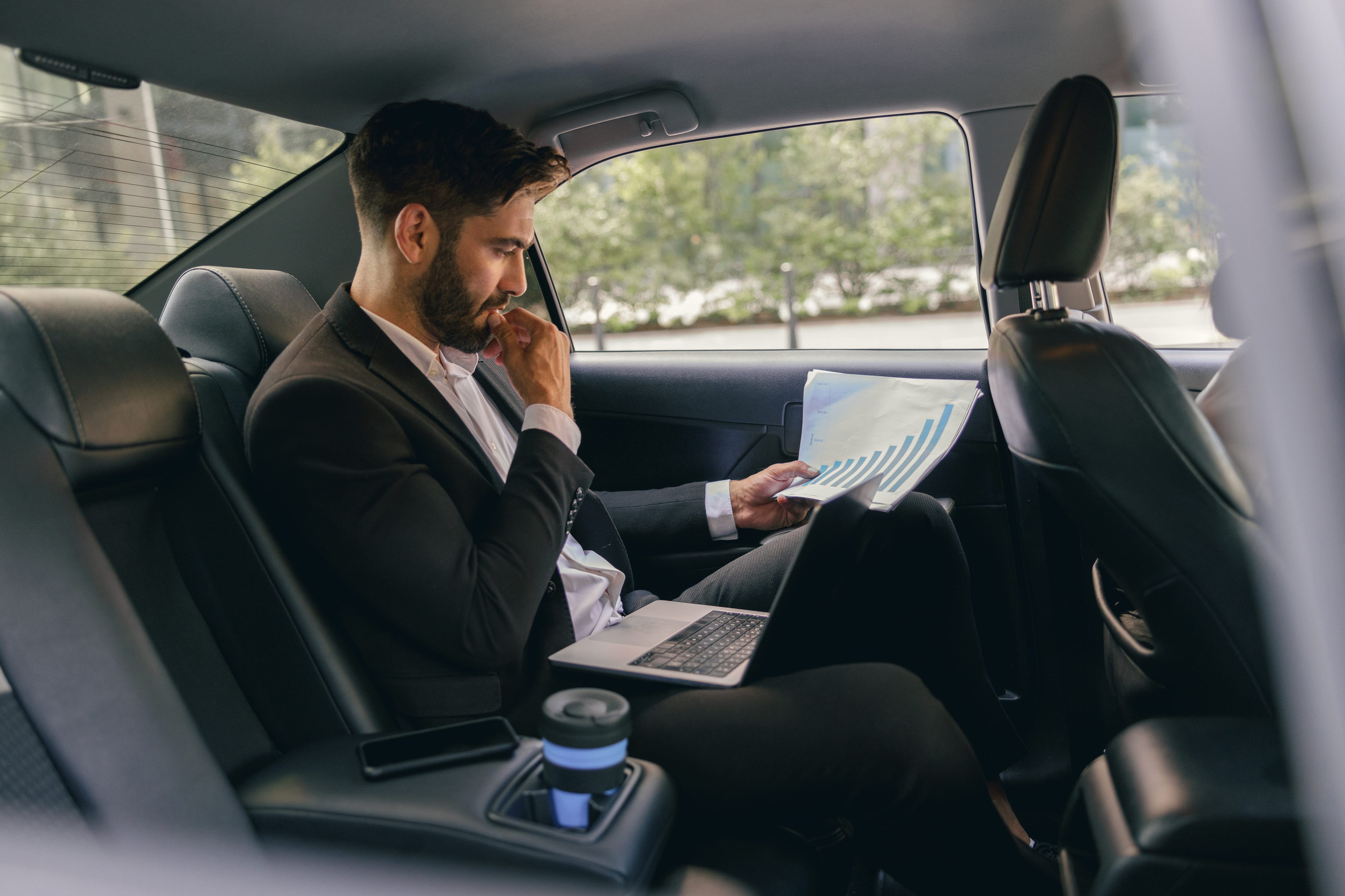 Confidence businessman sitting on car backseat and working with documents while going to office